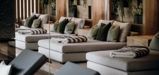 Rieser - Ruheraum Daybeds, Liegen in creme/weiß/grau, Zierkissen in unterschiedlichen grün Tönen, Felldecke, Pflanzen im Hintergrund